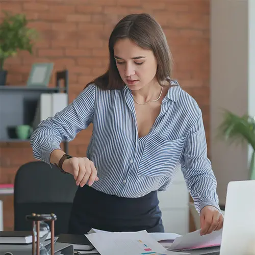 gestion du temps : une jeune femme très pressée dans son bureau regarde sa montre